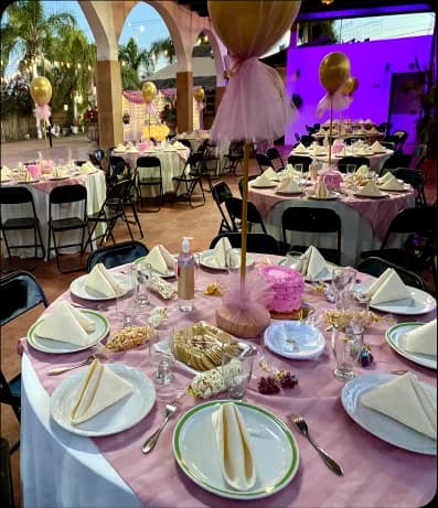 Mesas con cristalería, pequeñas bolsas de palomitas, galletas con un aderezo al centro, un pastel rosa y decoración en el centro.
