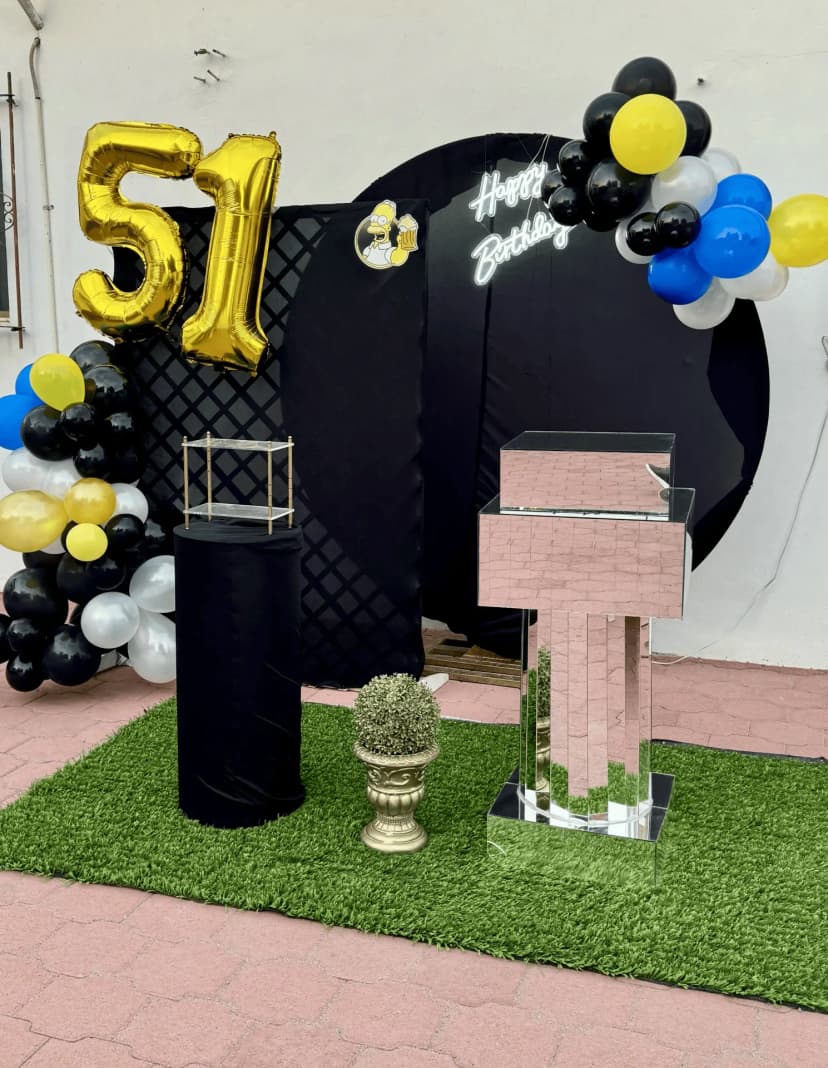 Mesa de honor número 13 con globos negros y dorados, temática divertida con un fondo negro y una imagen de Homero Simpson.