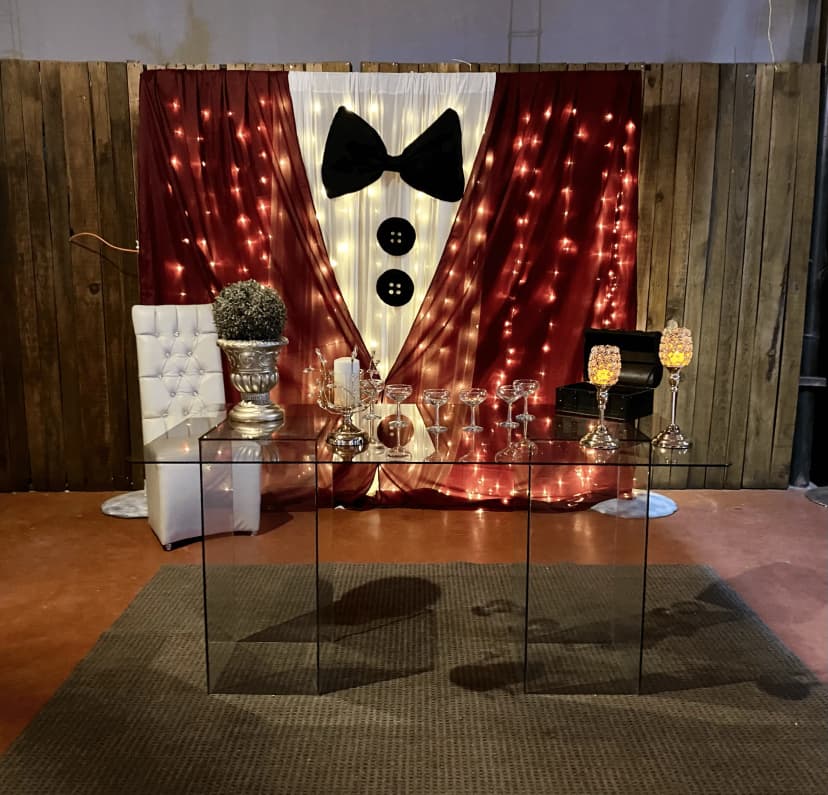 Mesa de honor número 18 con fondo que imita un smoking, mesa decorada con copas, velas y un elegante centro de mesa.