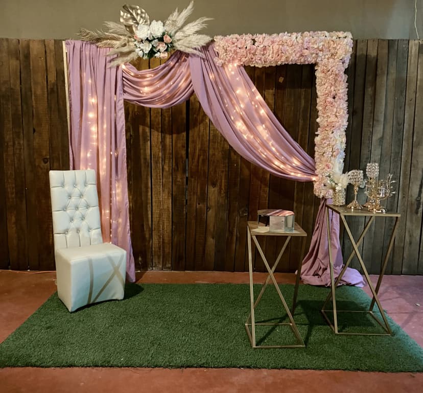 Mesa de honor número 19 con fondo rosa y luces, decorada con sillas blancas y mesas de madera con detalles elegantes.