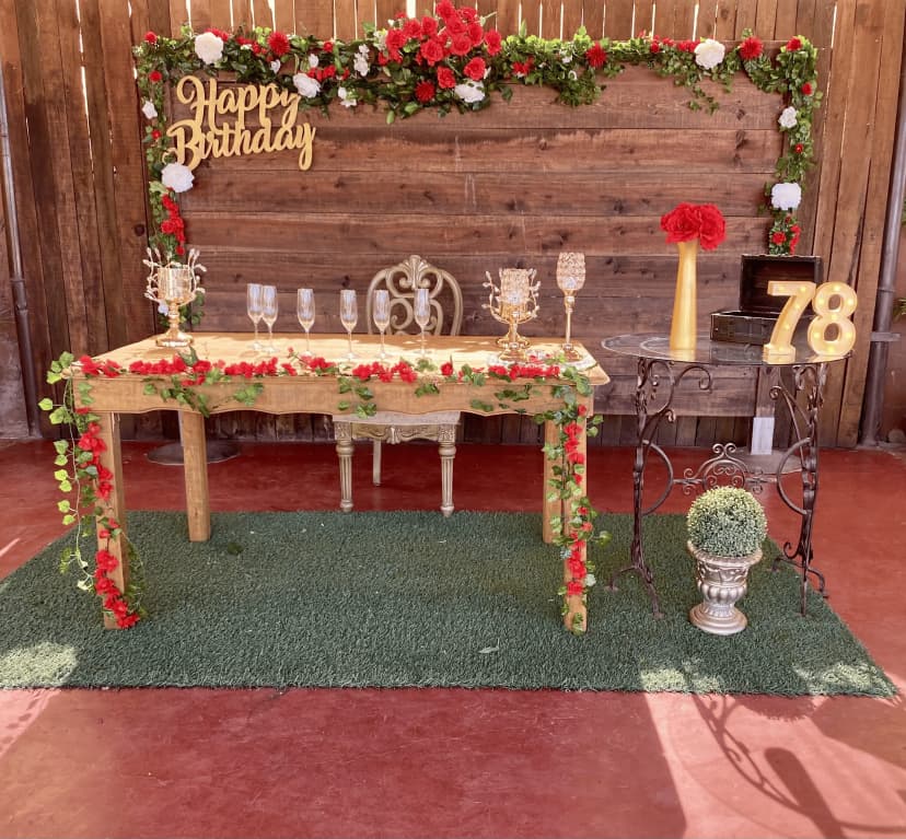 Mesa de honor número 20 con fondo de madera y letras "Happy Birthday", decorada con flores verdes, rojas y blancas.