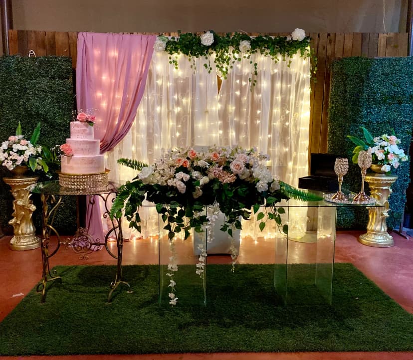 Mesa de honor número 23 con fondo blanco y rosa, decorada con flores y un pastel rosa en una mesa adicional al lado izquierdo.