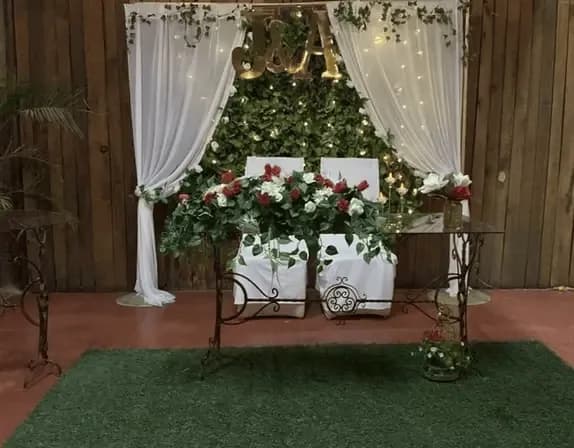 Mesa de honor número 5 con fondo de hojas verdes y rosas rojas y blancas, creando un ambiente natural y sofisticado.
