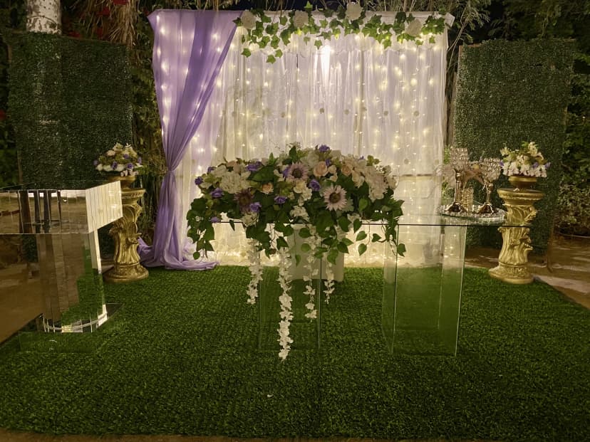 Mesa de honor número 6 con fondo blanco y morado, adornada con hojas verdes y flores en tonos blancos y morados para un estilo fresco.