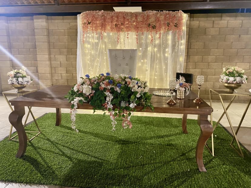 Mesa de honor número 7 con un fondo blanco y rosa, decorada con hojas verdes y flores en tonos blancos y rosas, con iluminación cálida.