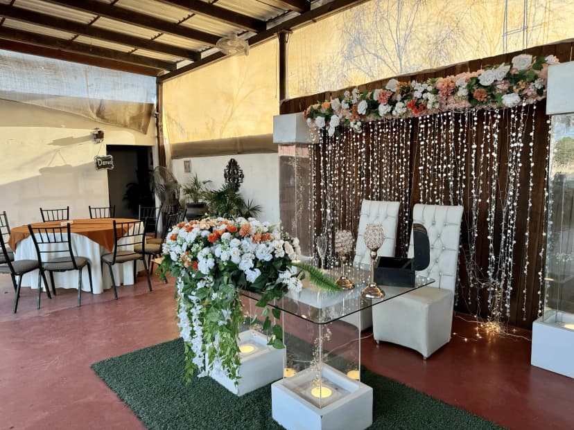 Mesa de honor número 9 con un fondo de luces y flores, decorada con un arreglo de hojas verdes y rosas en tonos blancos y salmón.